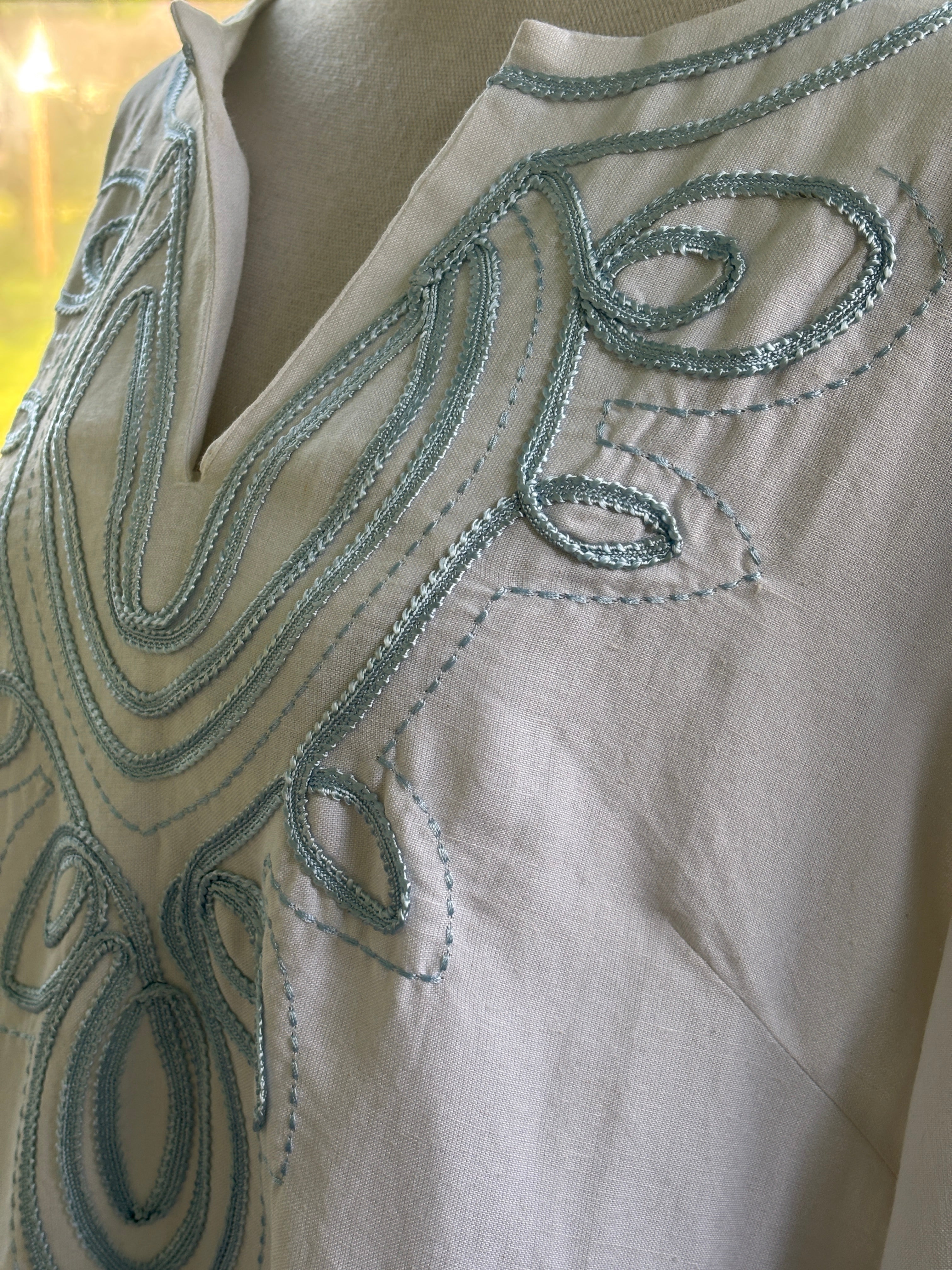 Close-up of sky blue scrolling embroidery detail at neckline on white ramie-rayon tunic dress by Les Canebiers