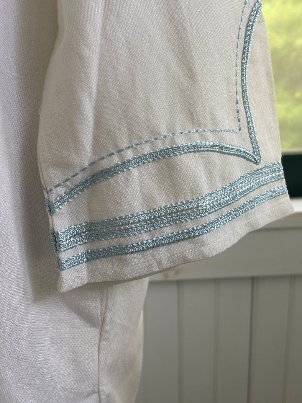 Close-up of sky blue embroidered trim detail at cuff of Les Canebiers white tunic dress