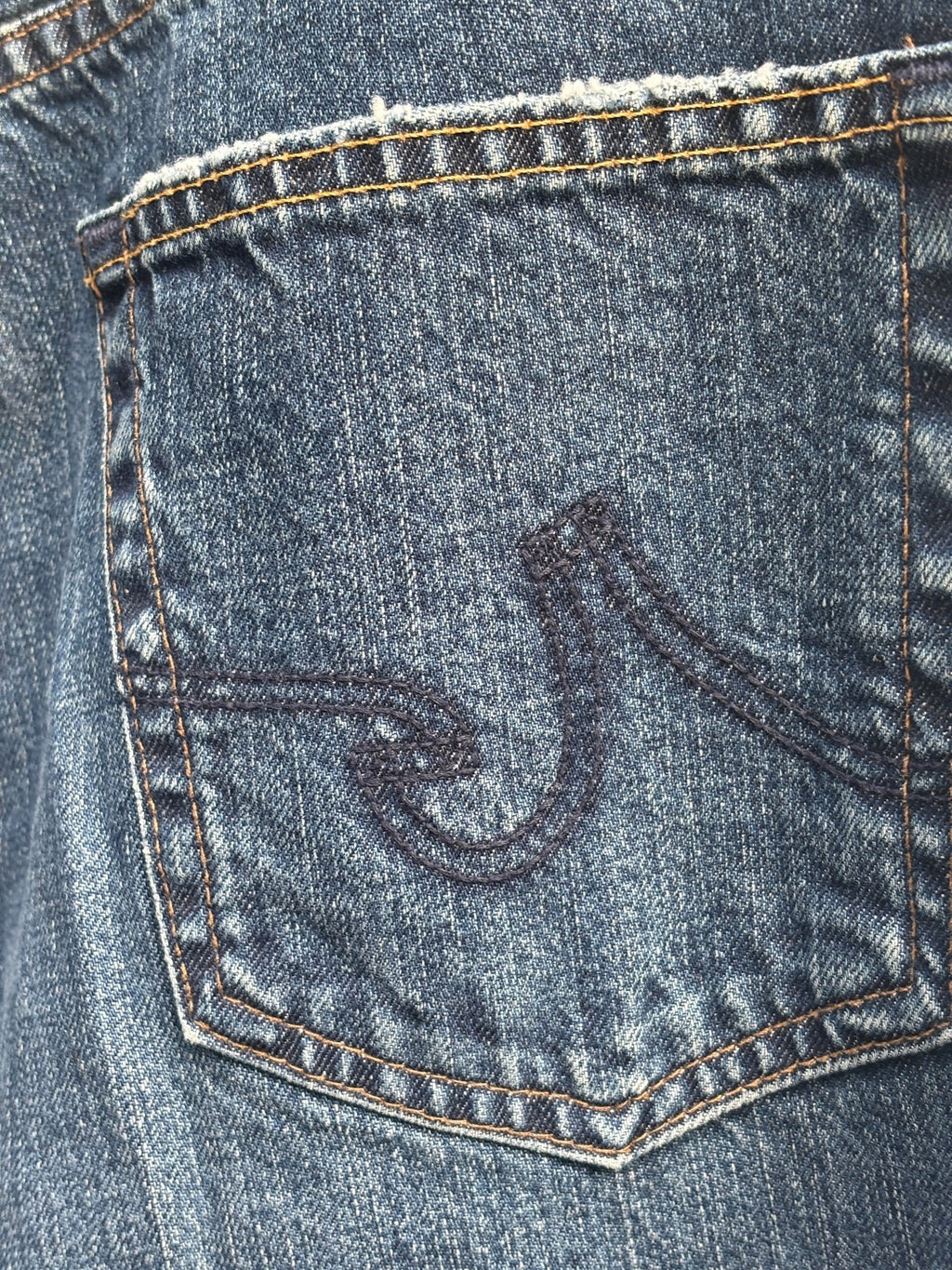 Close-up of embroidered AG logo on back pocket of distressed jeans