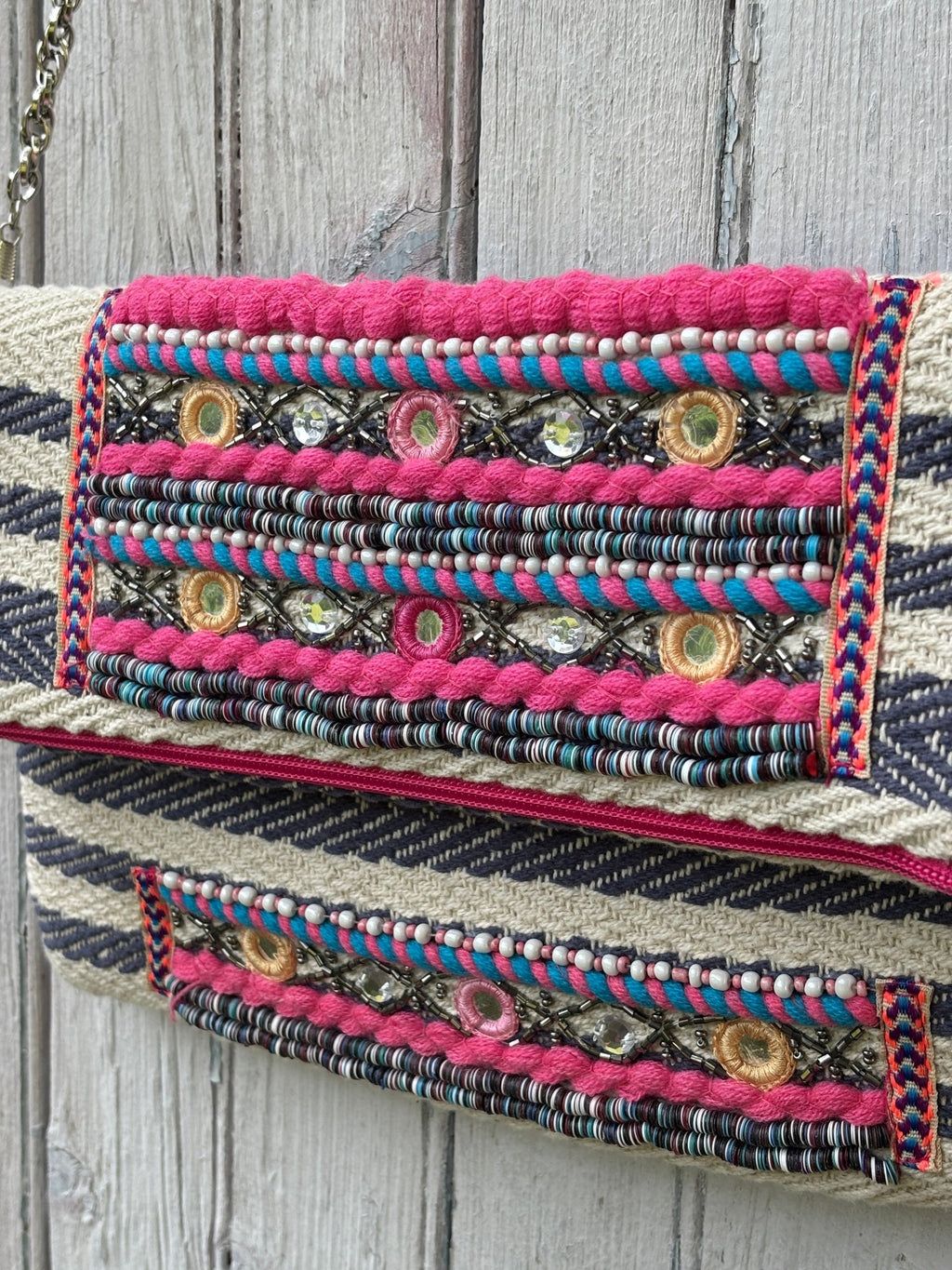 Close-up of pink yarn trim, seed beads, mirror embellishments and rhinestone detail on America & Beyond tribal fold-over clutch flap