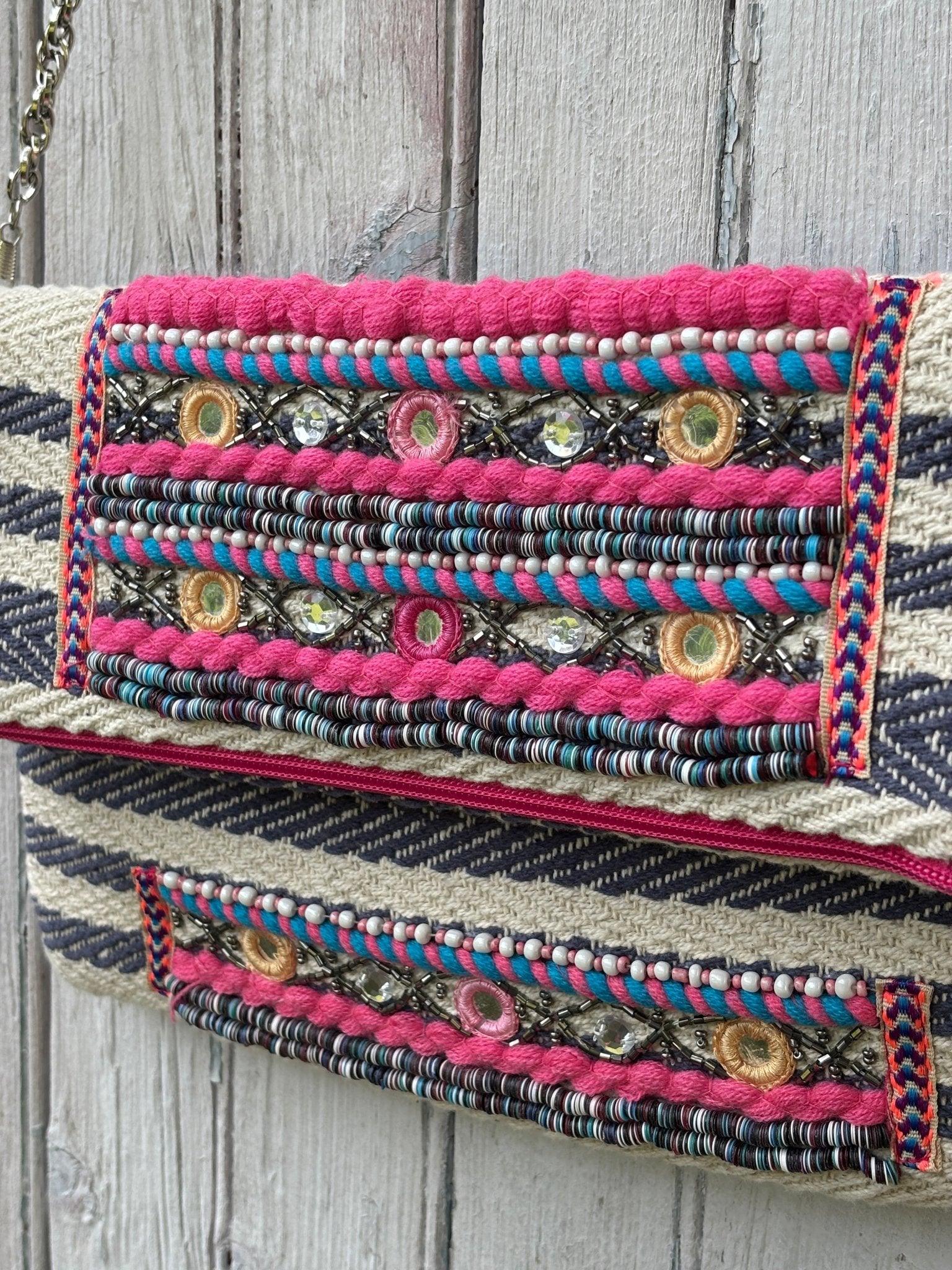 Close-up of pink yarn trim, seed beads, mirror embellishments and rhinestone detail on America & Beyond tribal fold-over clutch flap
