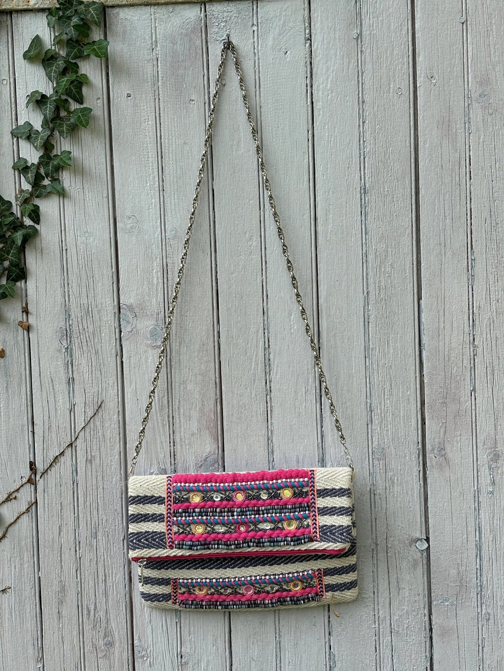 America & Beyond tribal embellished fold-over clutch bag hanging on fence with silver chain strap, navy and cream herringbone body, like new