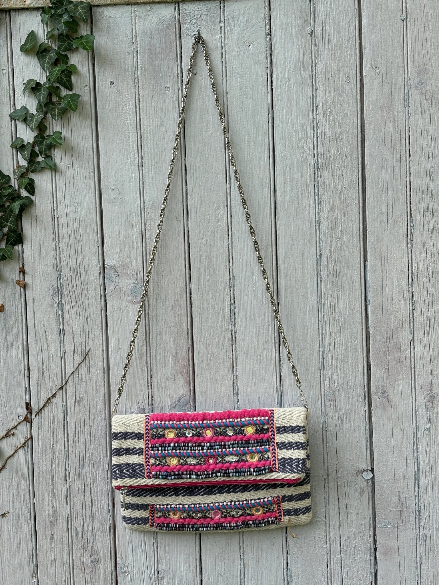 America & Beyond tribal embellished fold-over clutch bag hanging on fence with silver chain strap, navy and cream herringbone body, like new