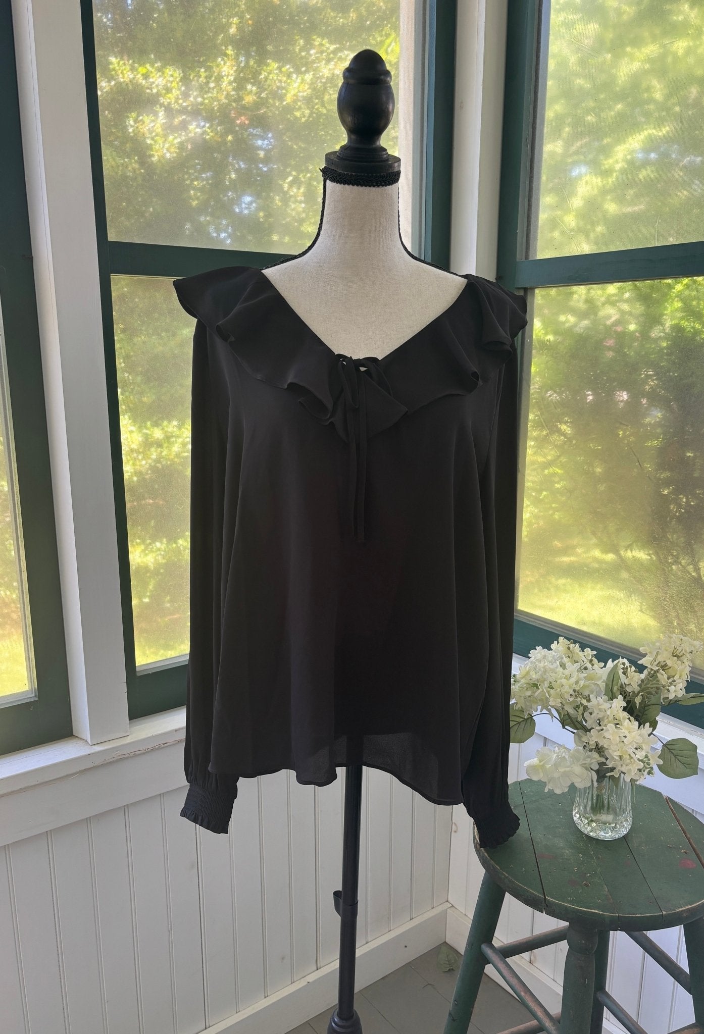 Ann Taylor black ruffle V-neck blouse on mannequin, wide ruffle collar with delicate self-tie and long flowing sleeves