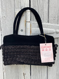Cupcake International black pompom purse hanging on weathered fence, dual velvet top handles and dense pompom body, NWT