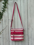 Dana Buchman red and cream stripe canvas crossbody bag hanging on weathered fence, adjustable red faux leather strap, like new