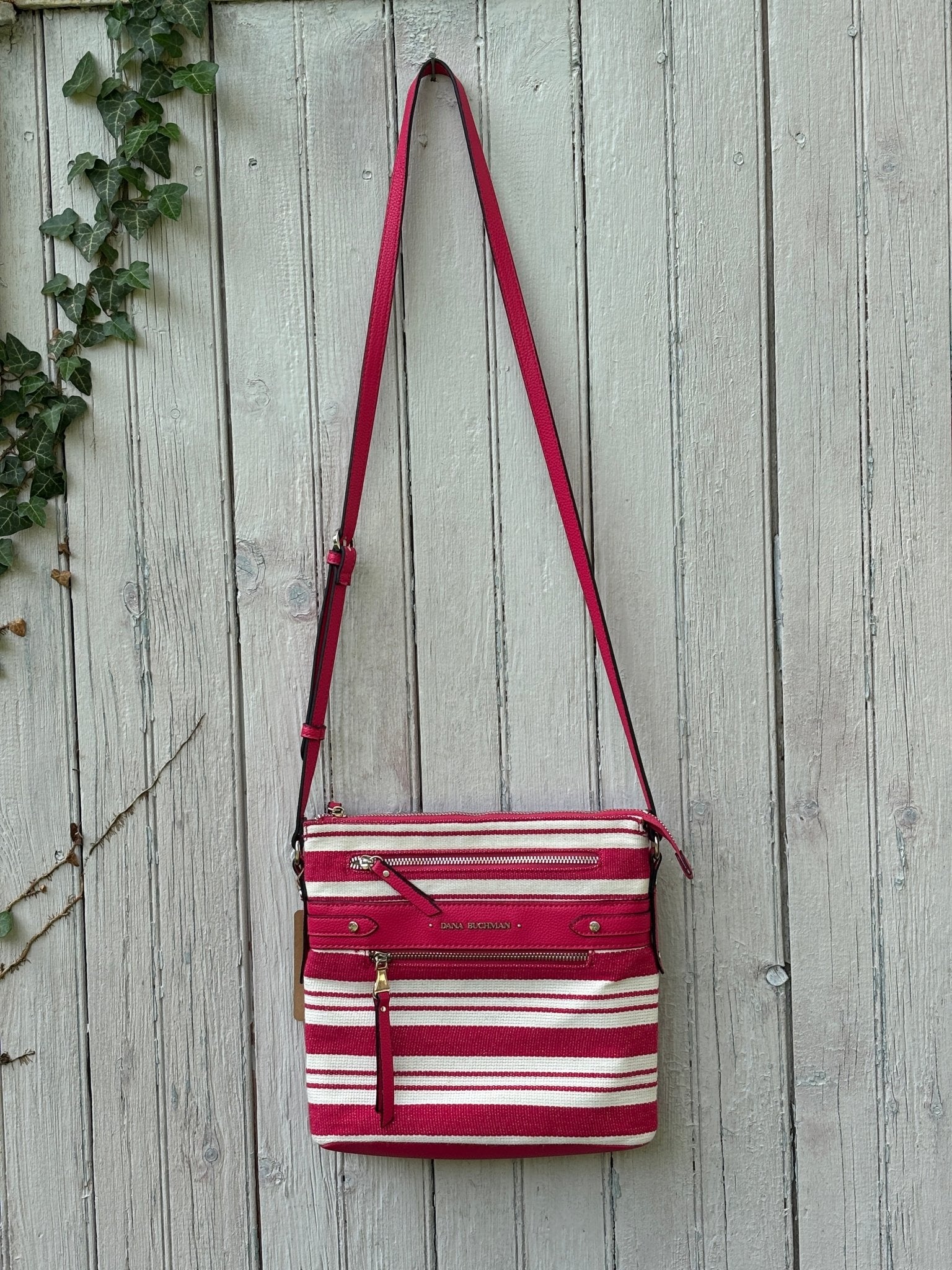 Dana Buchman red and cream stripe canvas crossbody bag hanging on weathered fence, adjustable red faux leather strap, like new