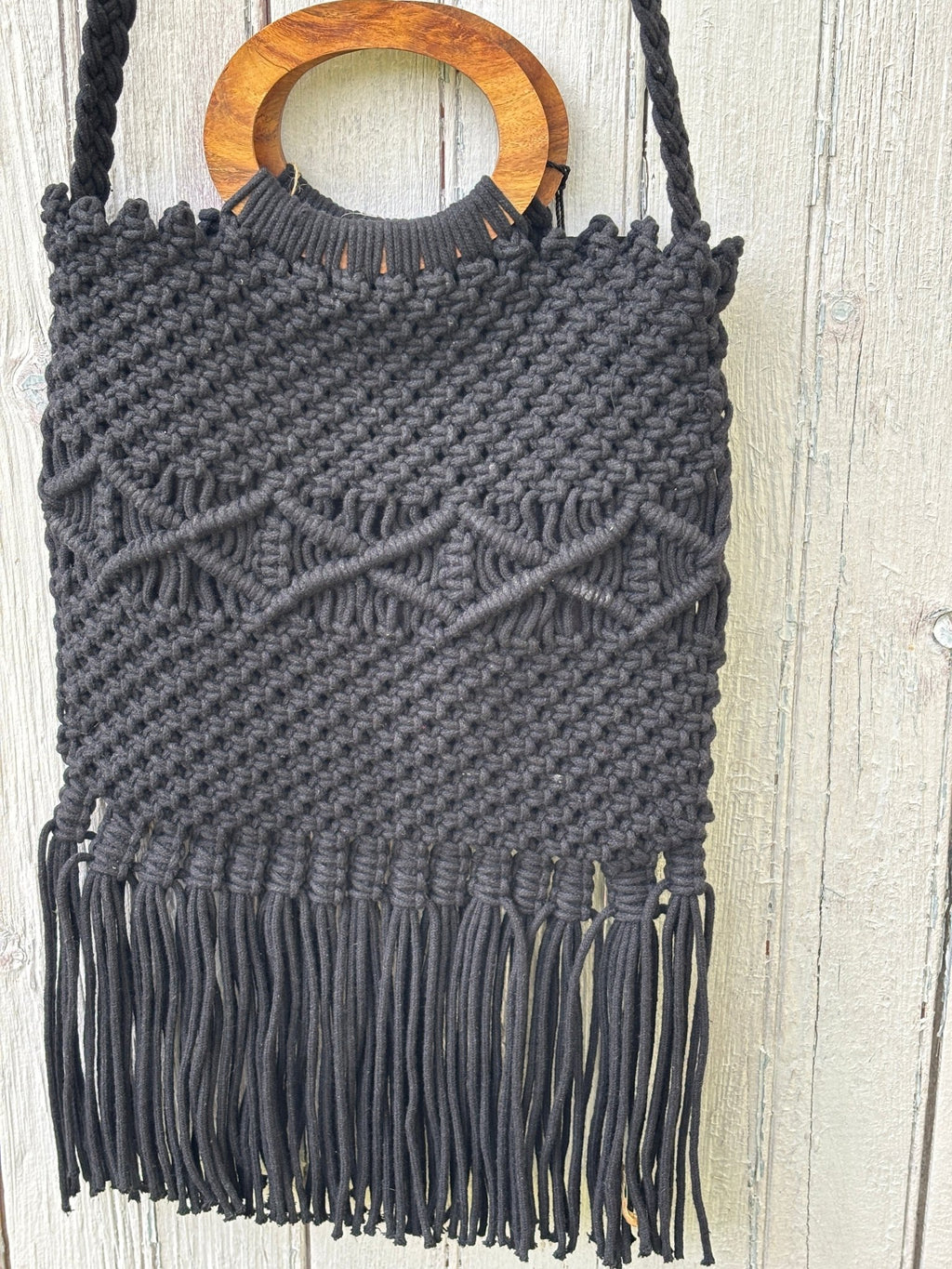 Close-up of round natural wood handle and dense fringe hem detail on Danielle Nicole black macramé tote