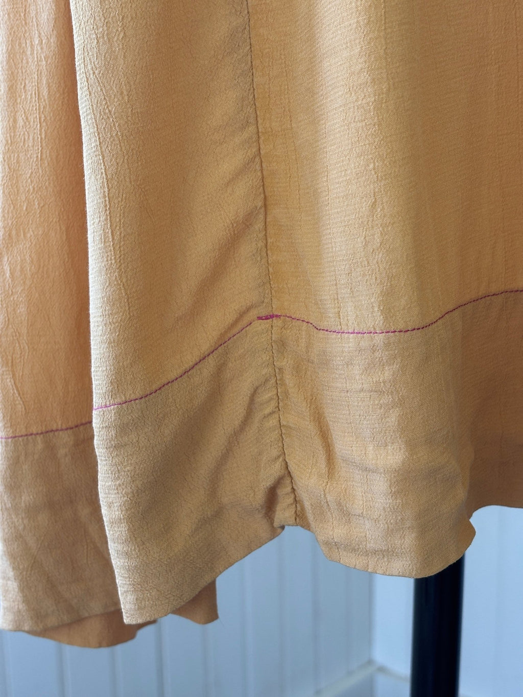 Close-up of curved pintuck hem and contrast stitch detail at lower dress
