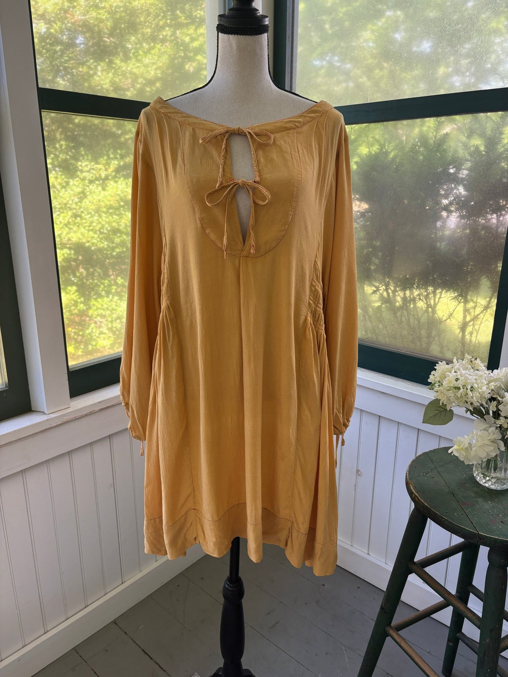 Front view of Free People Honey Honey long-sleeve mini dress in marigold on dress form, double-tie keyhole neckline, contrast pink topstitching visible