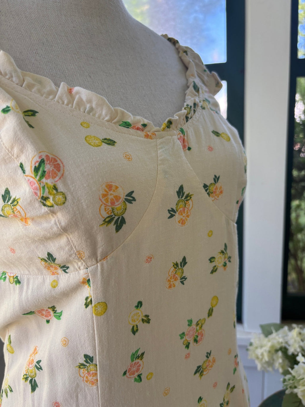 Close-up of Free People Like a Lady mini dress bodice showing ruffle cap sleeve, sweetheart neckline, and citrus lemon print on cream viscose-linen