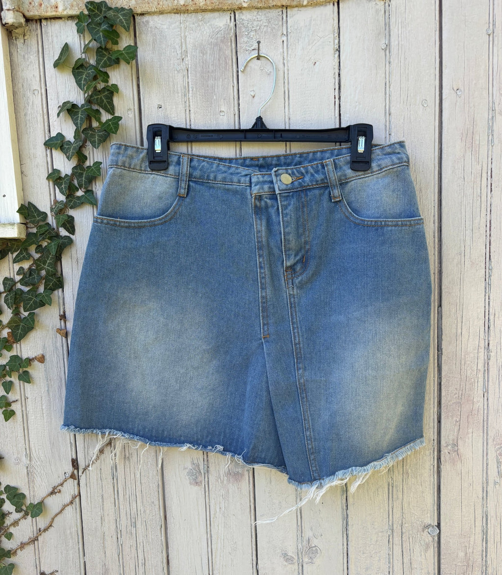 Hayden Los Angeles light wash denim wrap mini skirt on fence hanger, front view showing faux-wrap detail and raw frayed hem, size Large NWT