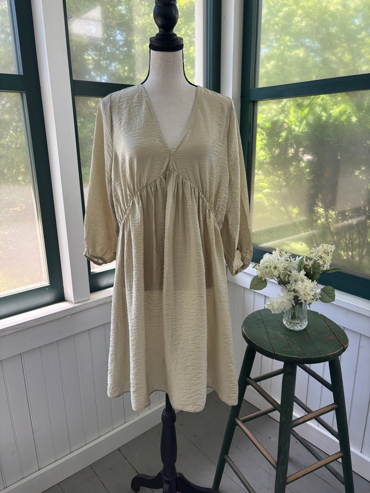 Front view of H&M Conscious sandy ecru crinkle viscose babydoll midi dress on dress form, deep V neckline, balloon sleeves, gathered empire waist
