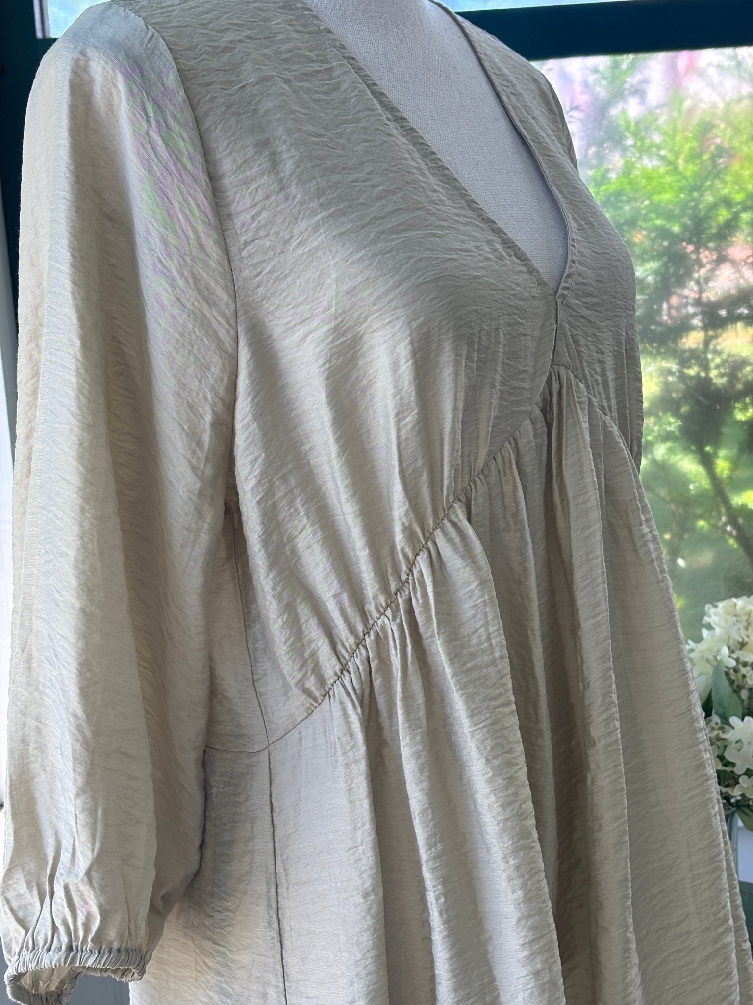 Close-up of front bodice showing V-neckline, crinkle texture, and gathered empire waist seam detail with balloon sleeve cuff