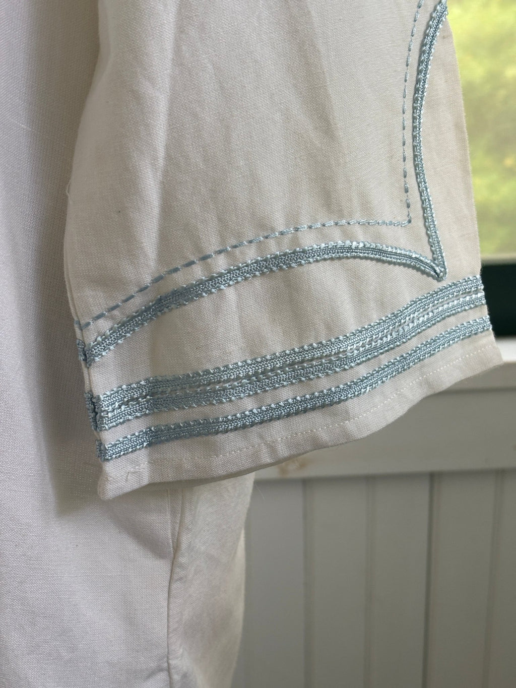 Close-up of sky blue embroidered trim detail at cuff of Les Canebiers white tunic dress