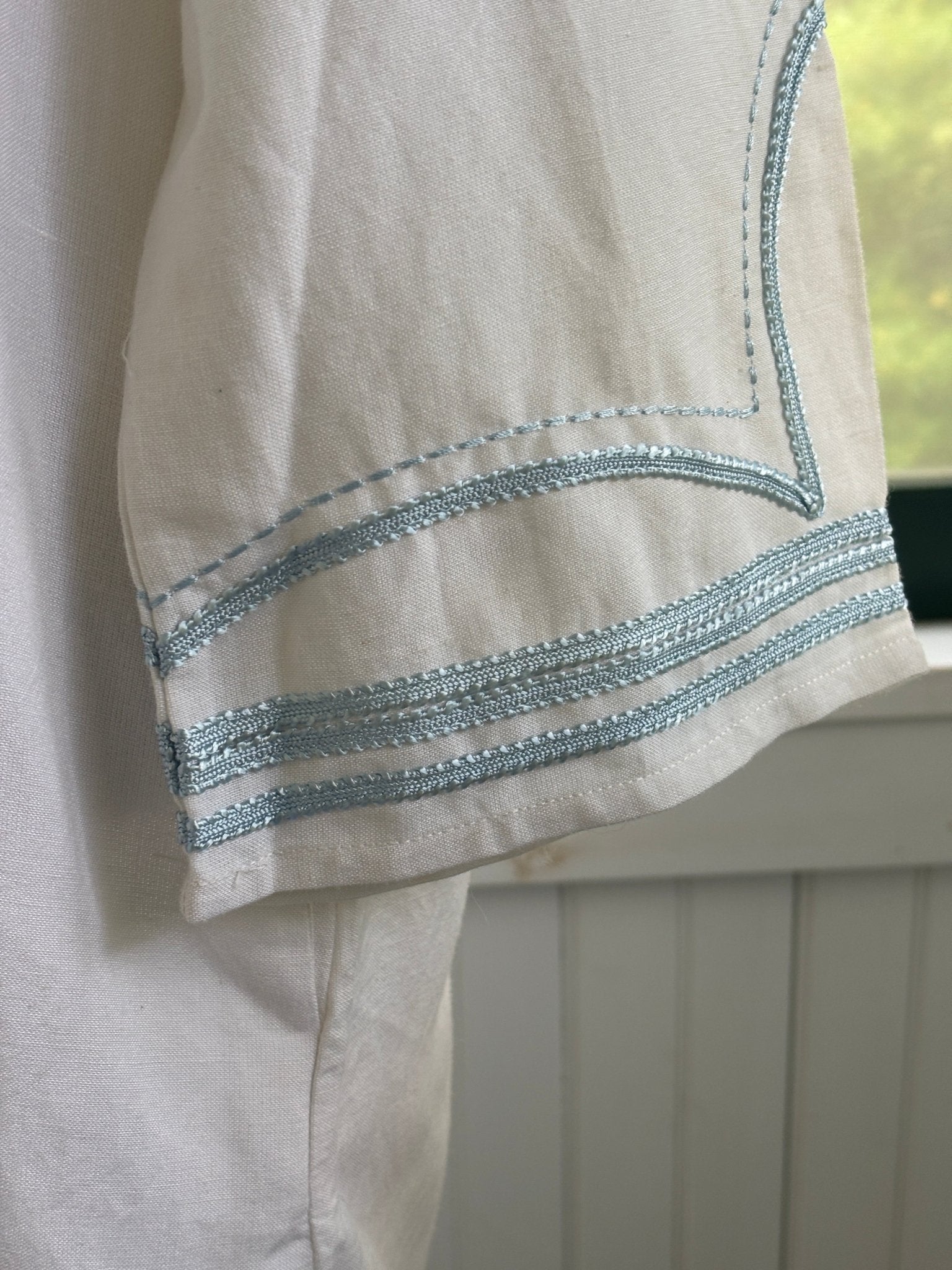Close-up of sky blue embroidered trim detail at cuff of Les Canebiers white tunic dress