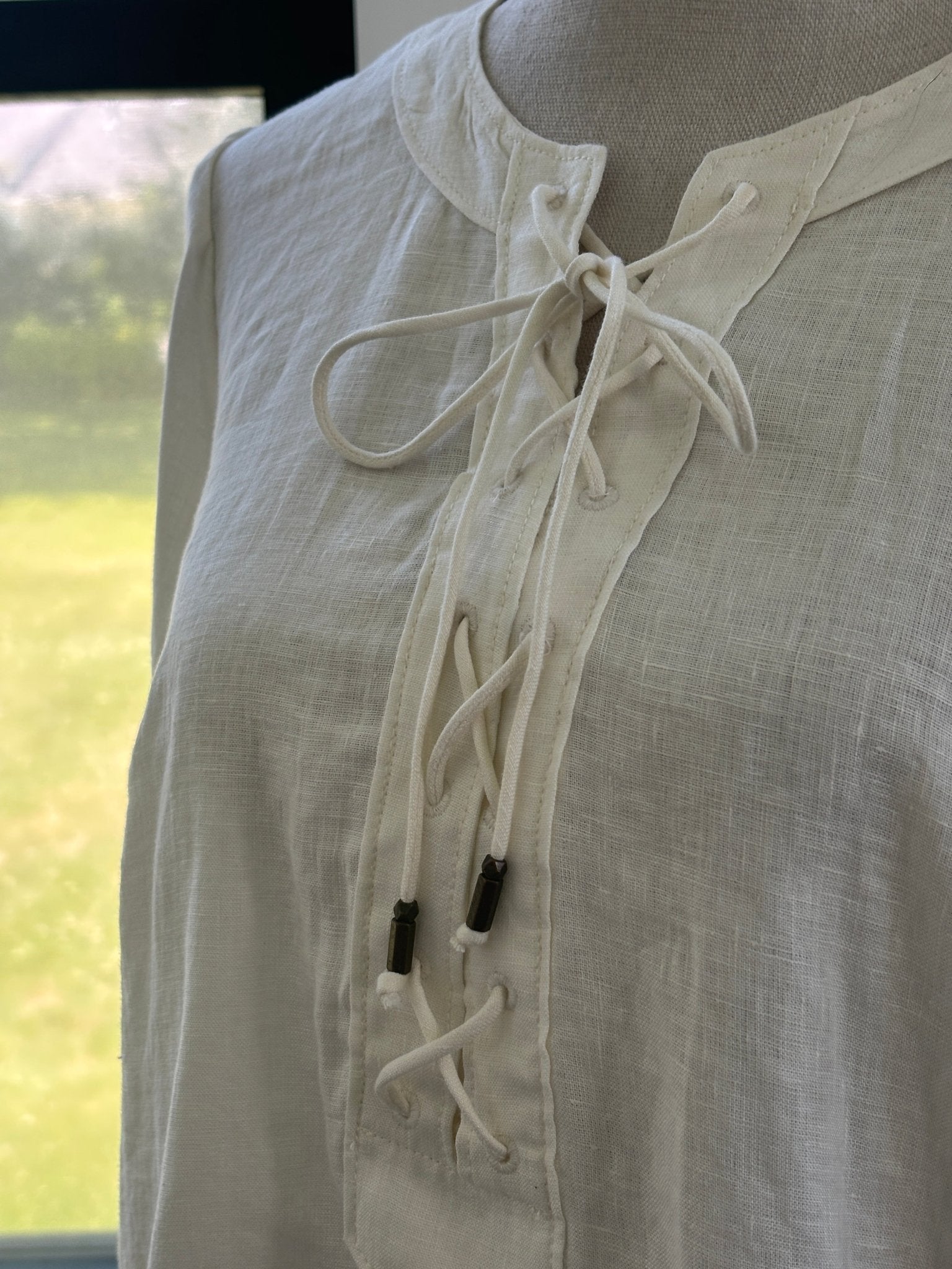 Close-up of corded lace-up neckline with dark metal aglet detail on Maeve by Anthropologie ivory linen top