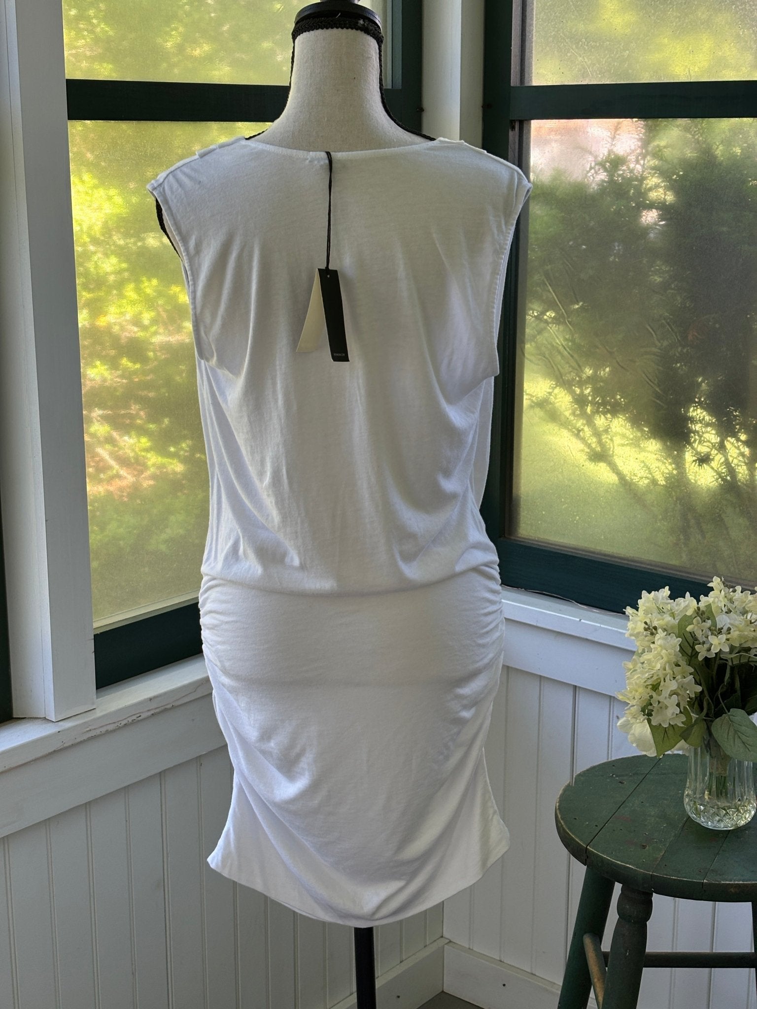 Back view of Monrow white ruched mini dress on mannequin with original black hang tag attached