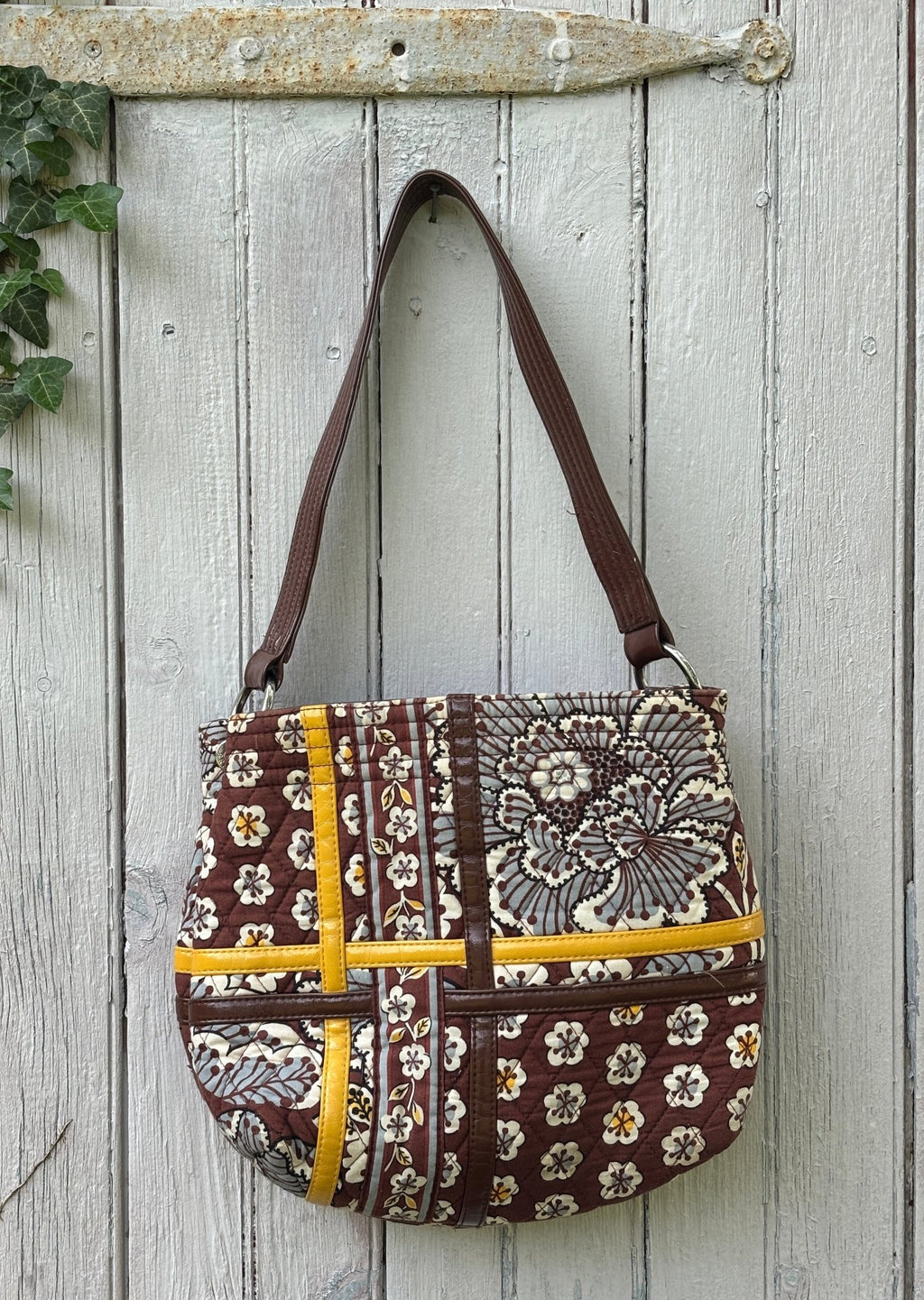 Back view of Vera Bradley brown floral patchwork quilted shoulder bag showing rounded silhouette and brown faux leather straps