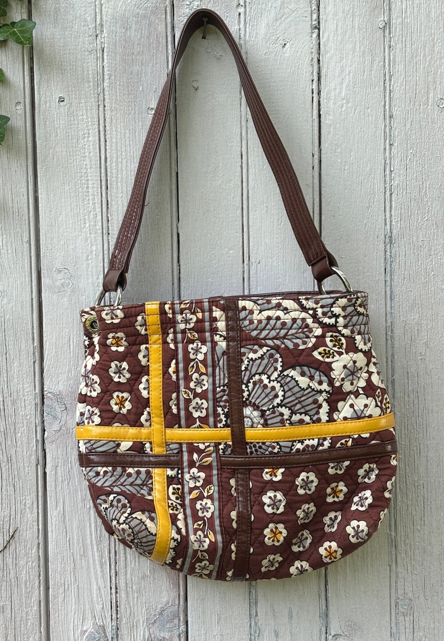 Vera Bradley retired brown floral patchwork quilted shoulder bag hanging on fence, mustard yellow and brown patent trim, like new